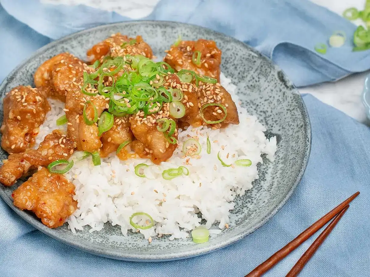 Krispig orange chicken med sesamfr&ouml;n och salladsl&ouml;k serveras p&aring; en b&auml;dd av vitt ris. En l&auml;cker asiatisk r&auml;tt.