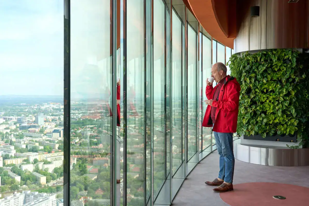 Mężczyzna w czerwonej kurtce pije kawę, podziwiając panoramę Wrocławia. Sprawdź sky tower wrocław cennik, by poznać ceny biletów.