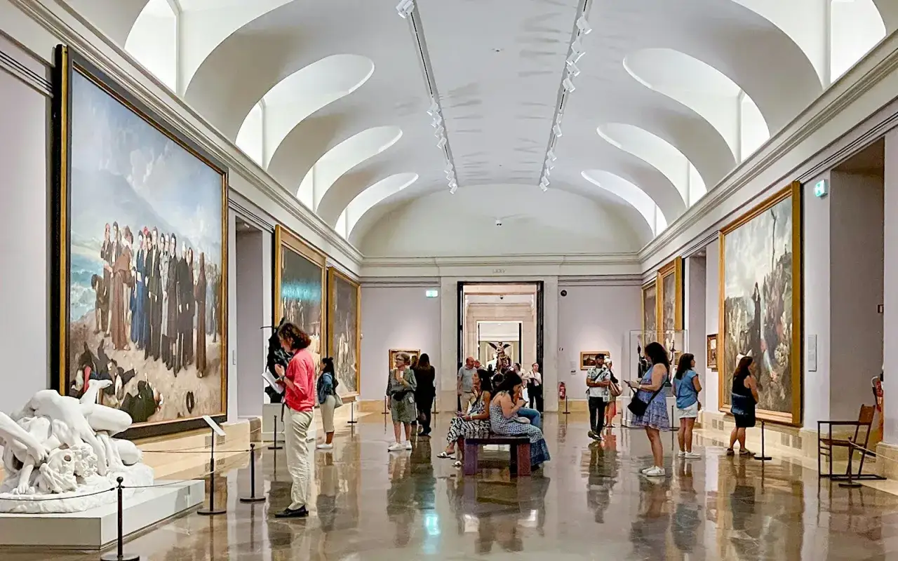 Besucher bestaunen Kunstwerke im Prado Museum in Madrid. Gro&szlig;e Gem&auml;lde und Skulpturen s&auml;umen die W&auml;nde des weitl&auml;ufigen Raumes.