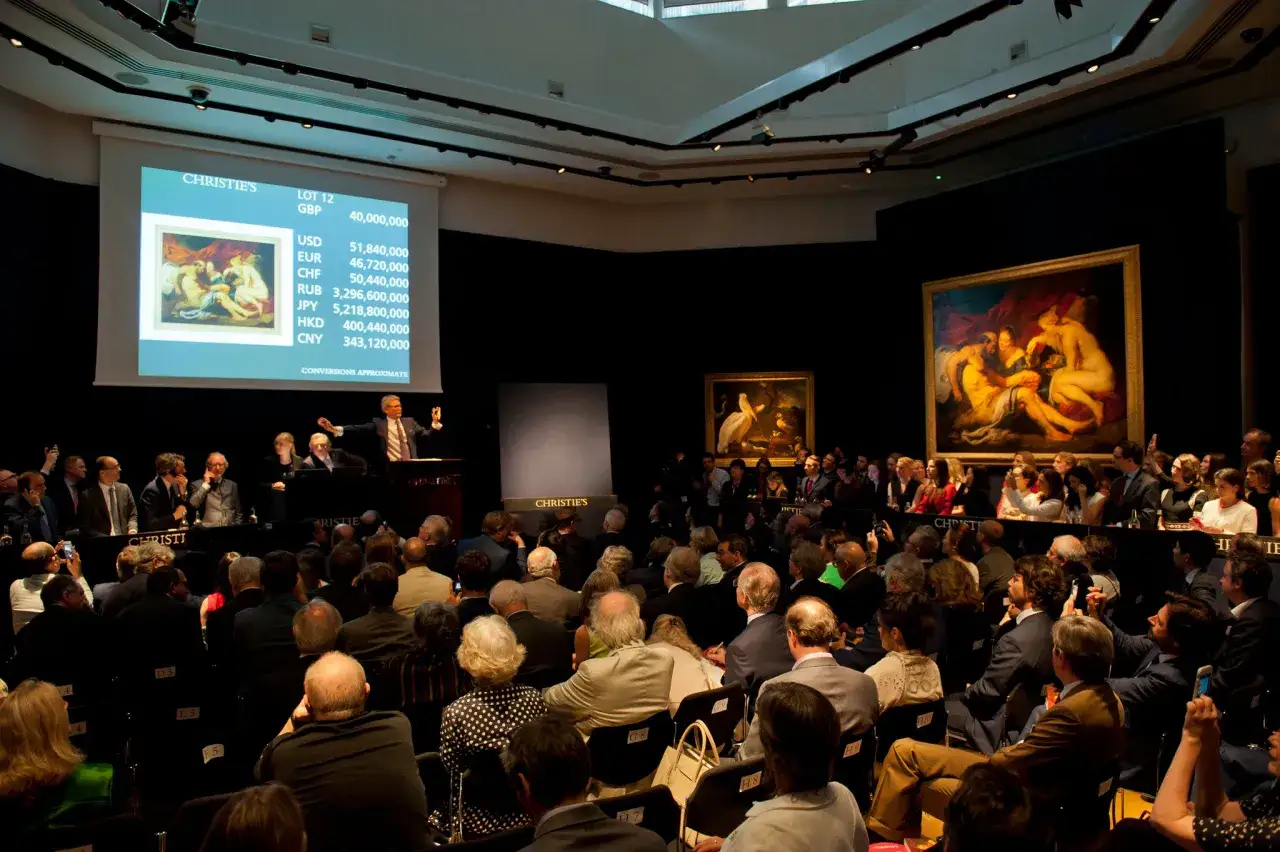 An auctioneer gestures at Christie's, with a screen displaying art lot details and prices, reflecting the dynamic contemporary art market.