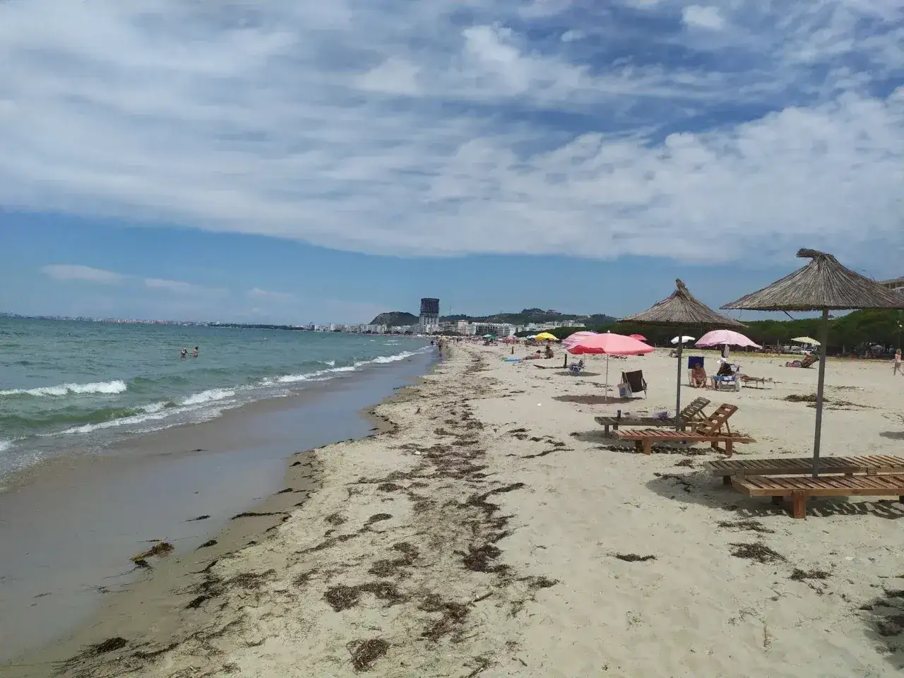 Plaża w Durrës, Albania, z leżakami i parasolami. W oddali widać miasto i morze.