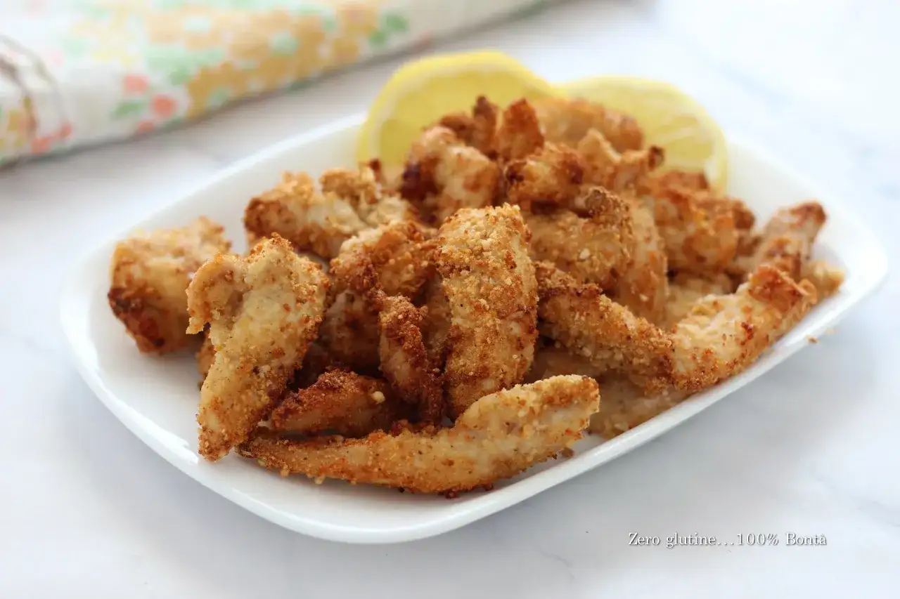 Straccetti di pollo in friggitrice ad aria, dorati e croccanti, serviti su un piatto bianco con spicchi di limone.