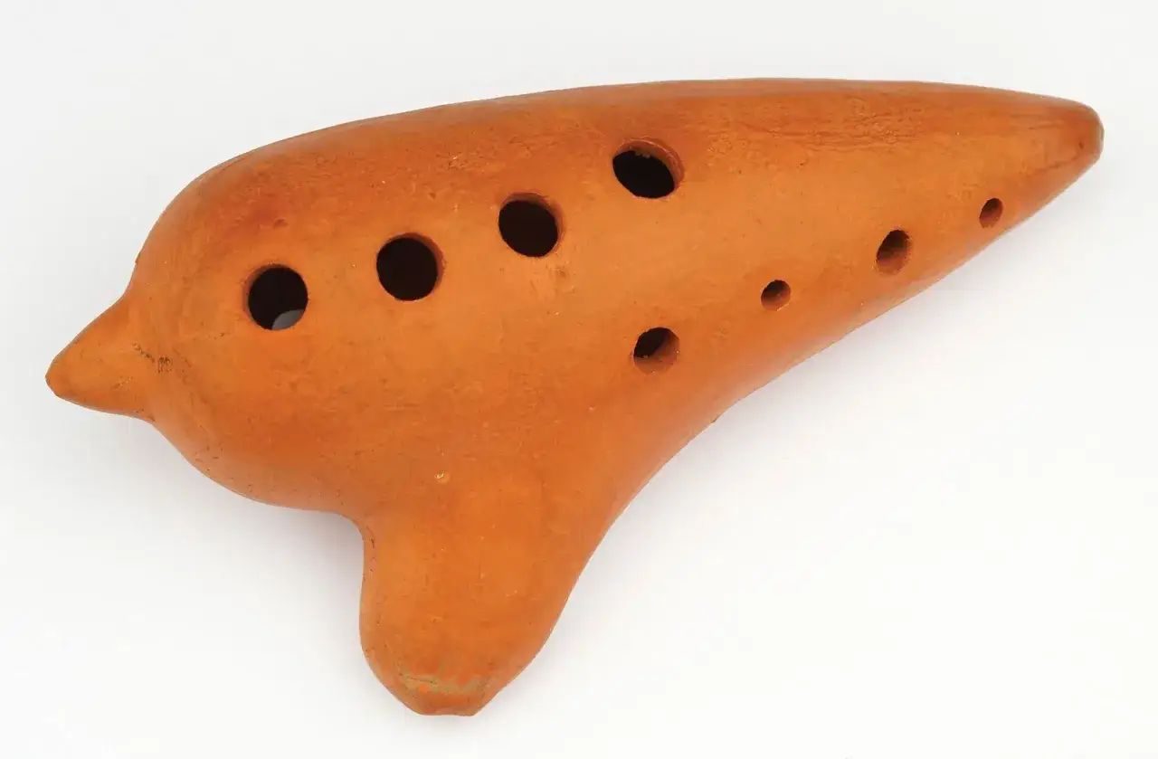 Orangefarbenes, tonartiges Musikinstrument mit vielen Löchern, das an eine Okarina erinnert.
