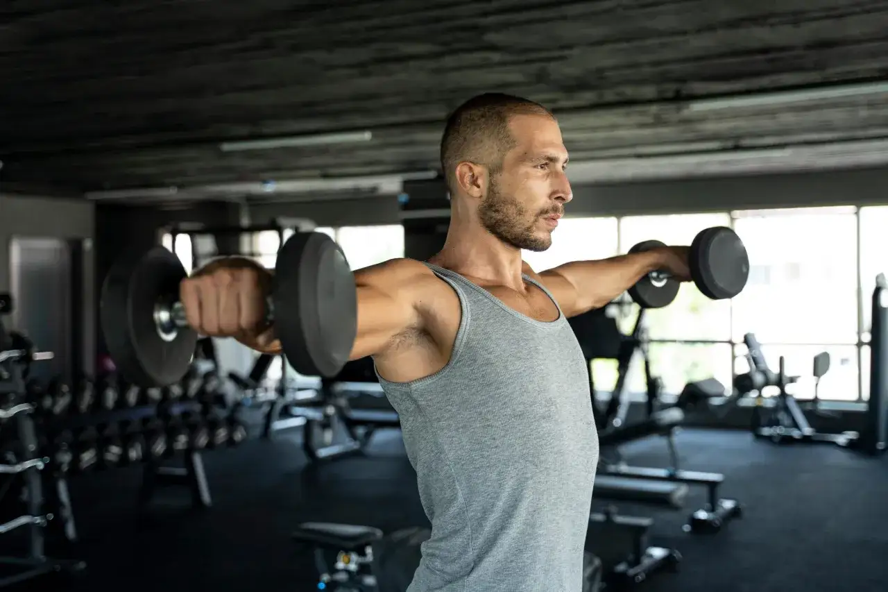 Mann hebt Hanteln im Fitnessstudio. Er nutzt das Gewicht zum Trainieren seiner Schultern und Arme.