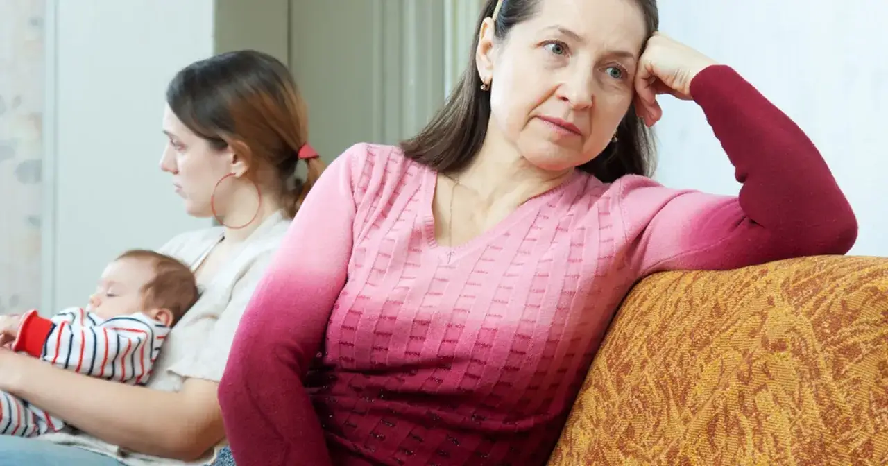 Smutna kobieta patrzy w dal, podczas gdy jej dorosłe dziecko tuli śpiącego niemowlaka.