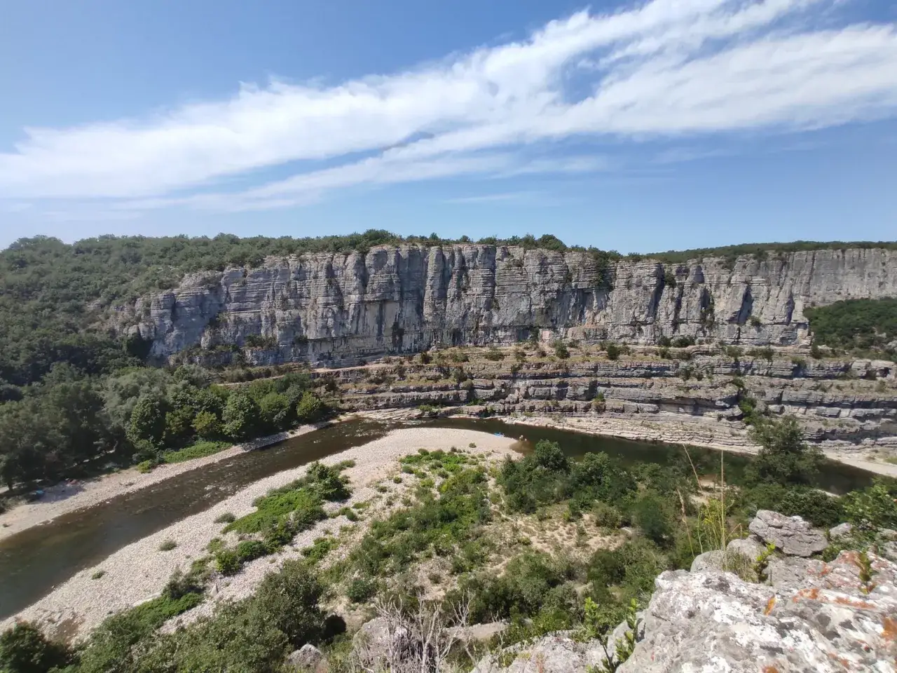 Le cirque de gens, un paysage spectaculaire de falaises calcaires sculptées par la rivière Ardèche, sous un ciel bleu parsemé de nuages.