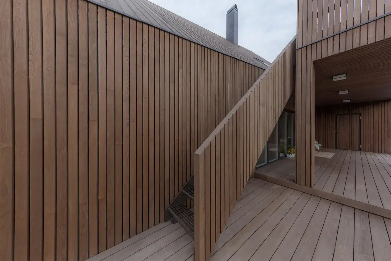 Moderne Architektur mit Fassaden und Terrassen aus thermisch modifiziertem Holz. Eine Außentreppe führt zu einem überdachten Bereich.