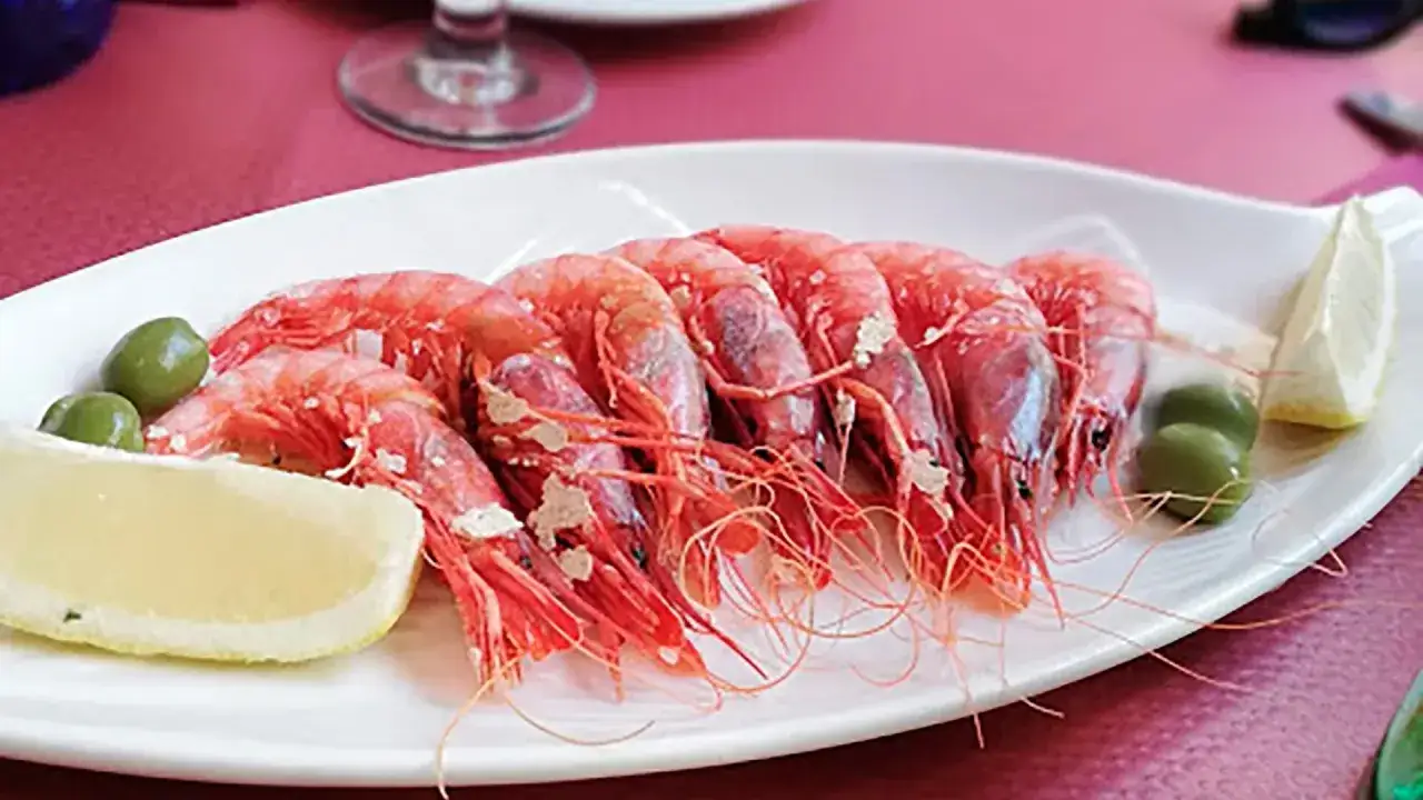 Deliciosos mariscos rojos, gambas frescas servidas con aceitunas y limón en un plato blanco.