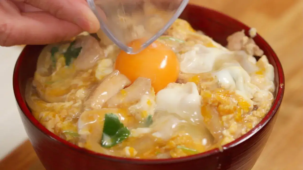 Ein rotes Sch&auml;lchen mit einem k&ouml;stlichen Oyakodon Rezept. Ein rohes Ei wird &uuml;ber H&uuml;hnchen und Reis gegeben.