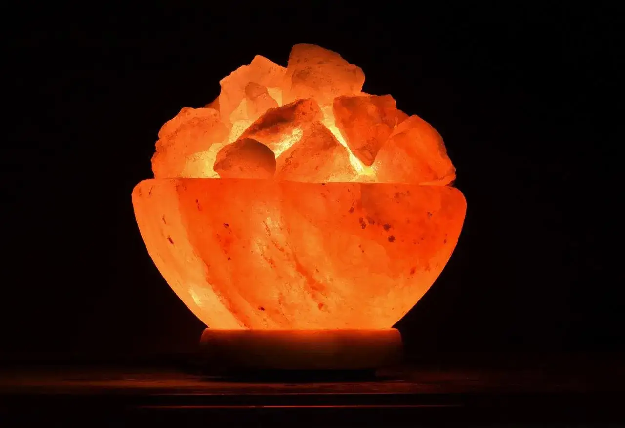 Lámpara de sal con trozos de sal rosa iluminados desde dentro, creando un ambiente cálido. Su diseño en forma de cuenco es ideal para controlar la humedad.