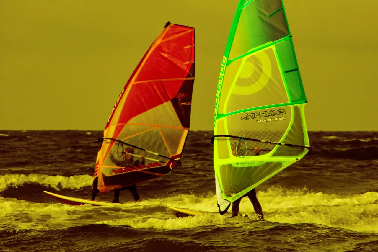 Zwei Windsurfer mit roten und grünen Segeln auf dem Meer. Ein aufregender Tag für Surf und Segel Hiddensee.