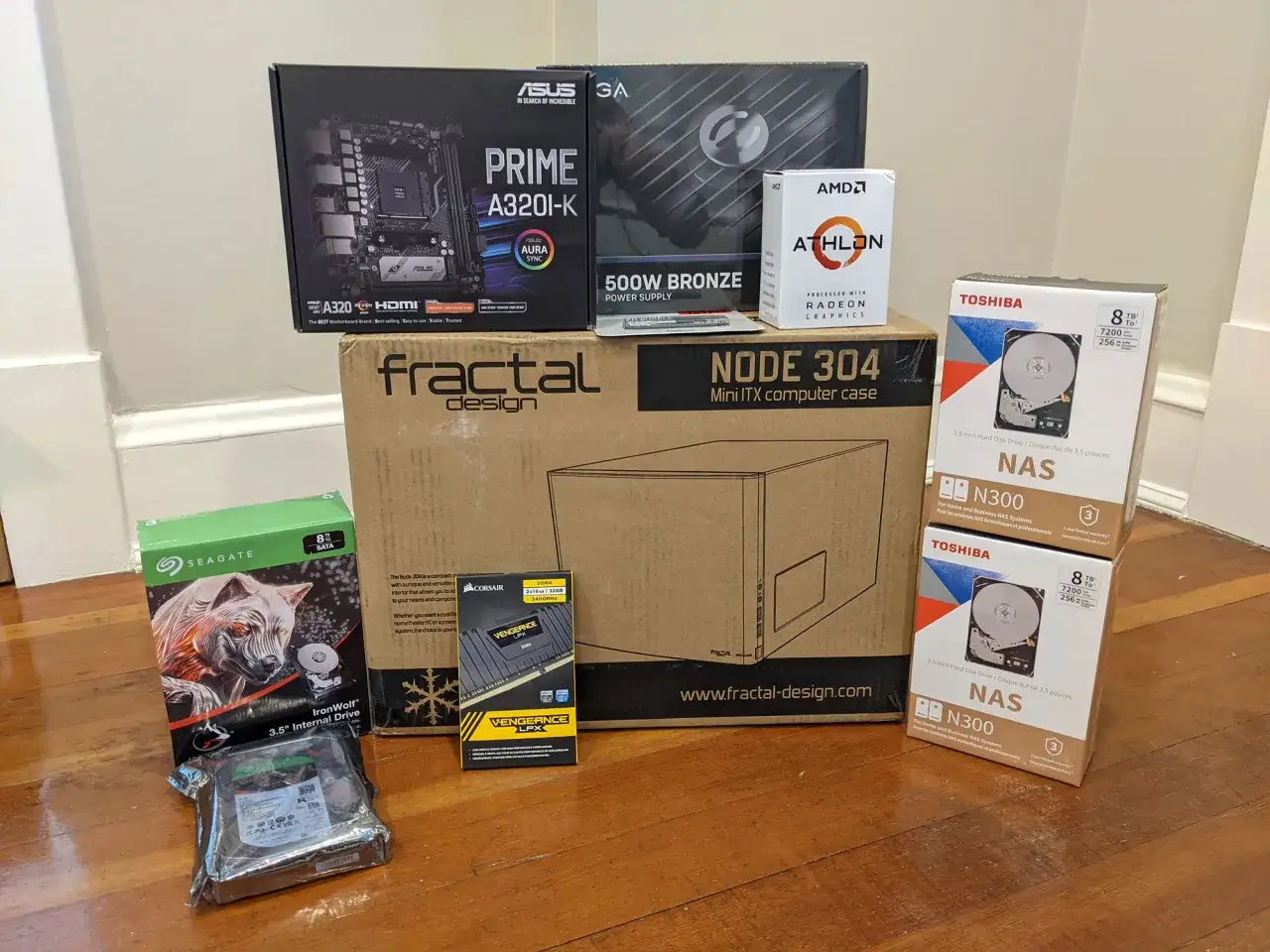 Composants pour installer un NAS : carte mère ASUS, processeur AMD Athlon, boîtier Fractal Design, alimentation, RAM Corsair, et disques durs Toshiba et Seagate.