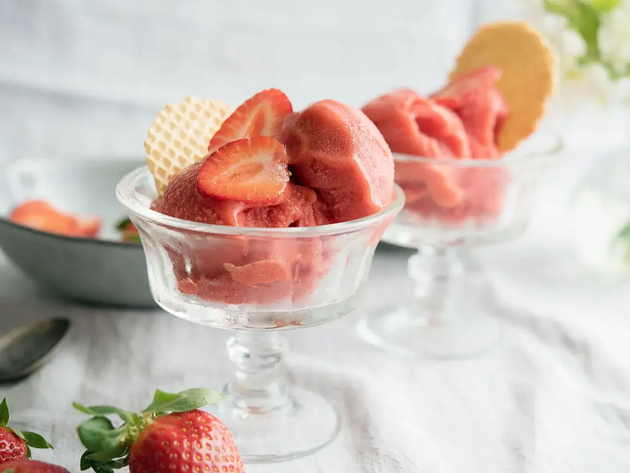 Zwei Gläser mit erfrischender Erdbeer Granita, garniert mit frischen Erdbeerscheiben und Waffeln.