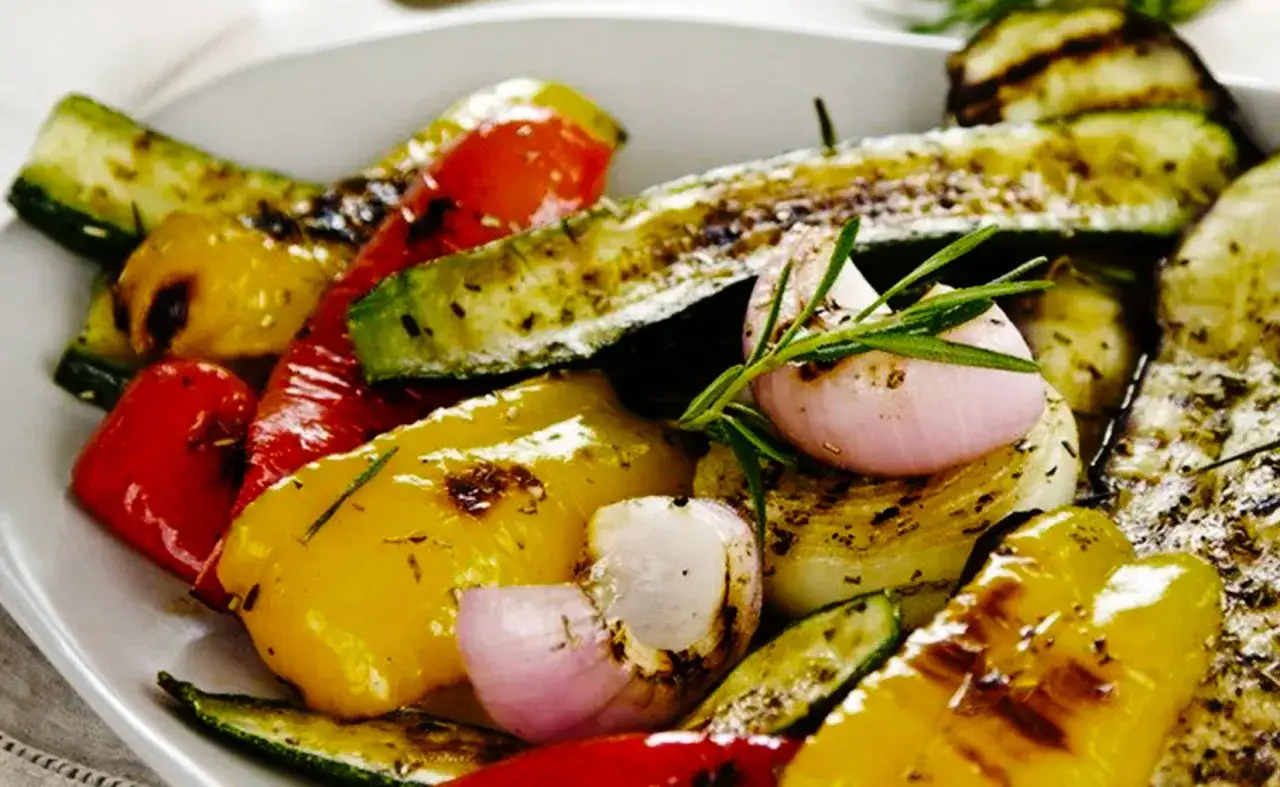 Assortiment de légumes à la plancha, marinés et grillés : courgettes, poivrons rouges et jaunes, oignons et échalotes, parsemés d'herbes.