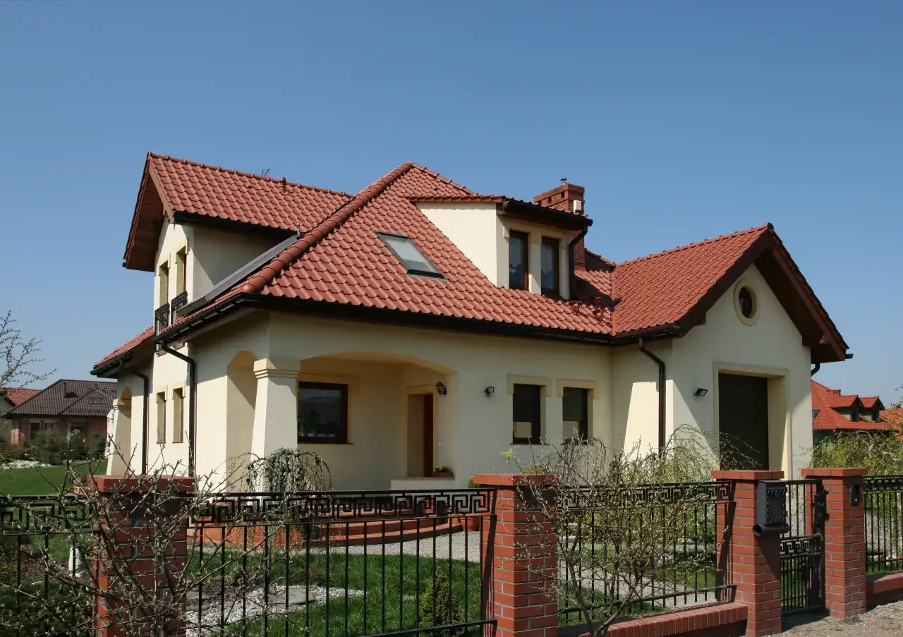 Nowoczesny dom z czerwoną dachówką i ogrodzeniem. Zastanawiasz się, jakie ogrzewanie wybrać do takiego domu?