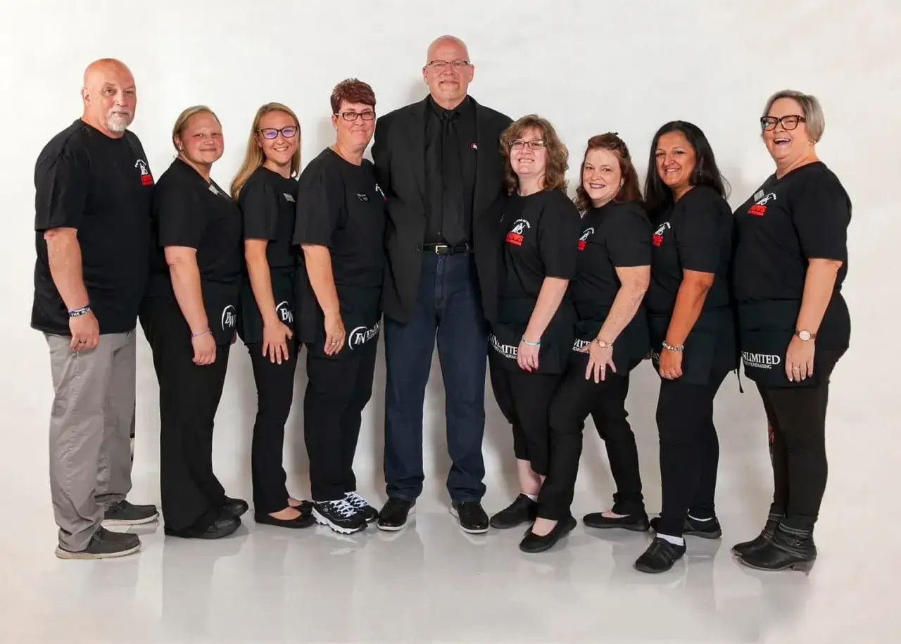 A team poses for a photo, ready for fundraiser planning. They wear matching black shirts and aprons, with one man in a suit.