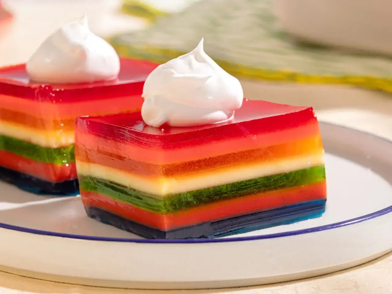 Postres arco&iacute;ris, un ejemplo de deliciosas recetas con gelatina. Capas de colores vibrantes coronadas con crema batida.