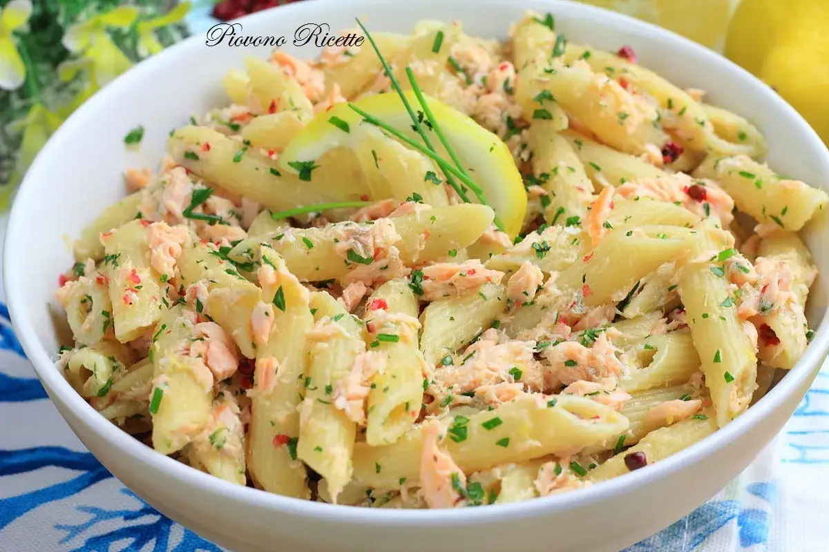 Pasta fredda con salmone affumicato, un piatto estivo fresco e saporito, guarnito con limone e prezzemolo.