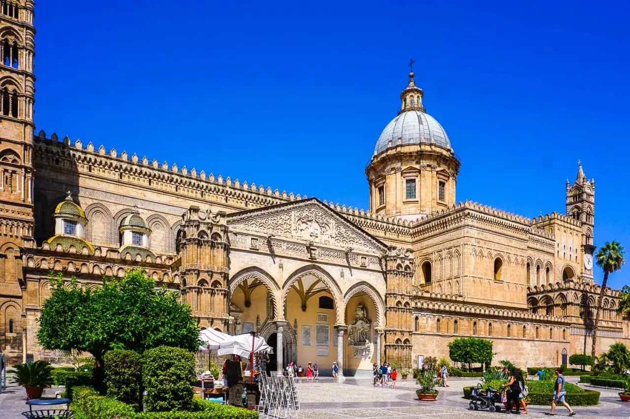 La maestosa cattedrale di Palermo, con le sue torri imponenti e la cupola dominante, si erge sotto un cielo azzurro.
