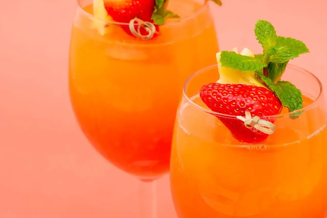 Deux verres de cocktail sans alcool anniversaire, d&eacute;cor&eacute;s de fraises, d'ananas et de menthe, sur fond rose corail.