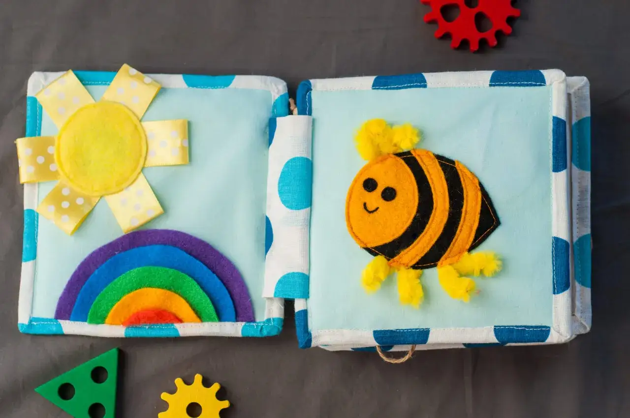 Libro de actividades de tela con un sol, arco&iacute;ris y abeja. Muchas cosas para hacer con telas y aprender.