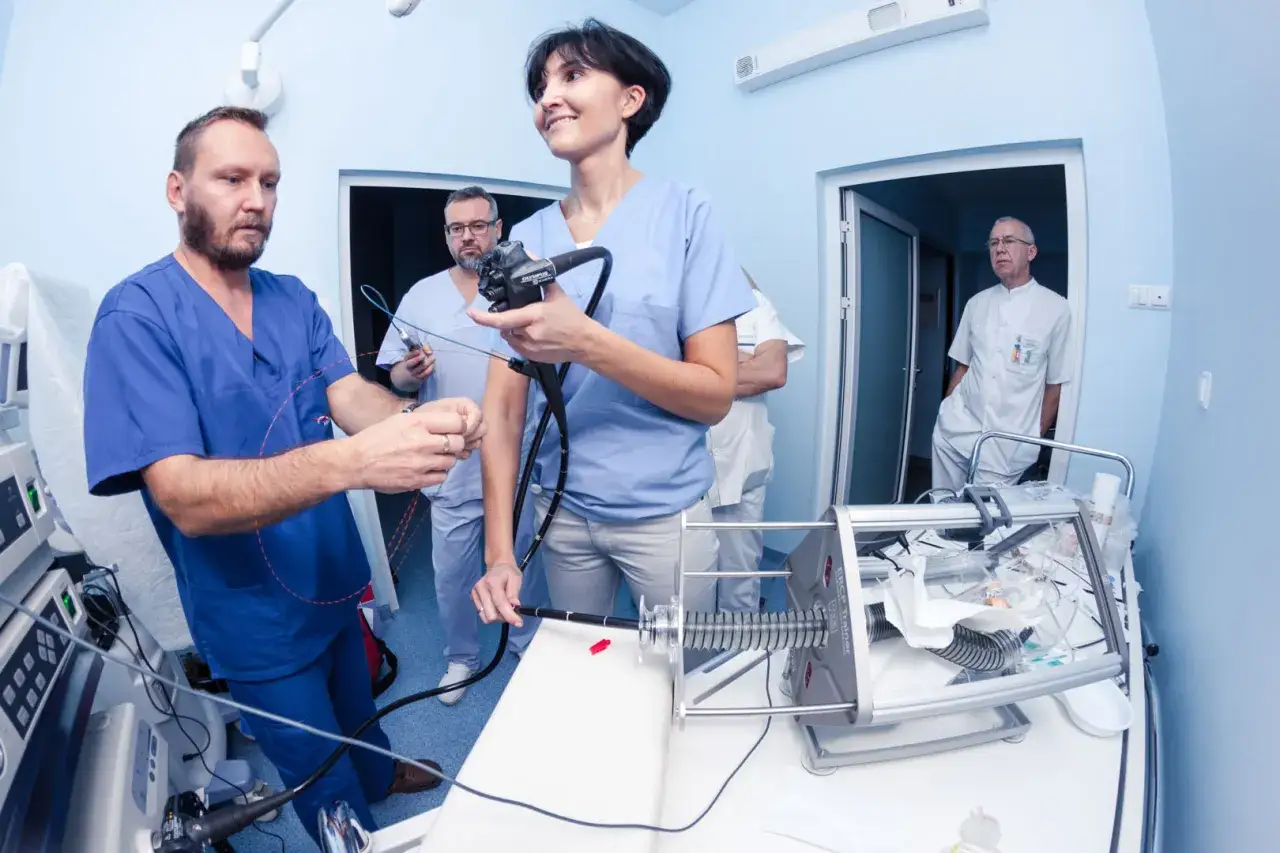 Pielęgniarki ćwiczą na symulatorze podczas kursu endoskopii. W tle lekarze obserwują.