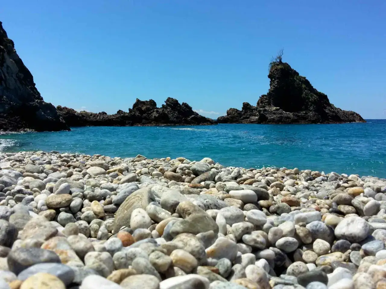 Spiaggia di ciottoli con scogli e mare cristallino, un angolo di paradiso a Reggio Calabria.