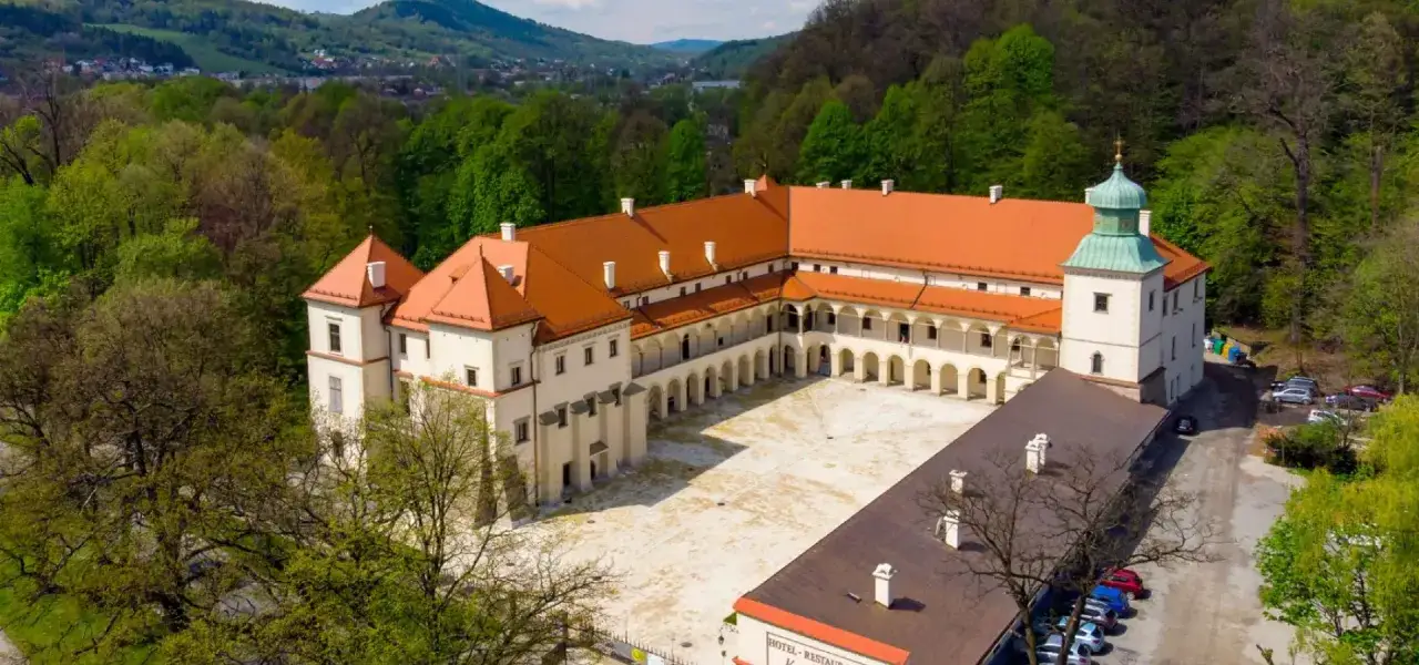Słynny Sucha Beskidzka zamek, otoczony zielenią, z dziedzińcem i wieżą.