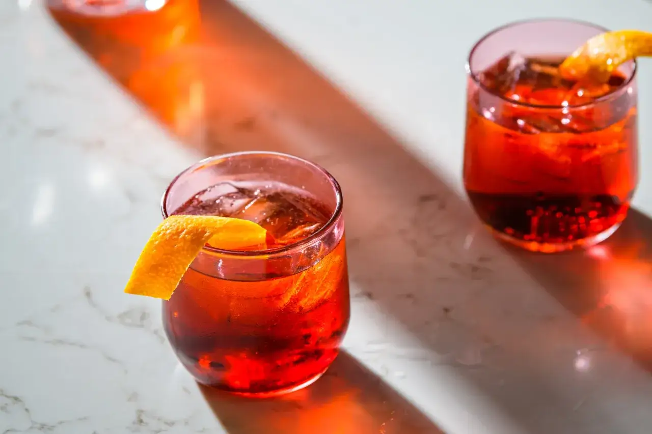 Zwei erfrischende Negroni-Cocktails mit Eis und Orangenzesten, bereit zum Genie&szlig;en. Die leuchtend roten Getr&auml;nke sind die perfekten negroni zutaten.