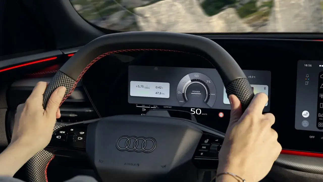 Ręce na kierownicy q5 audi. Na ekranie widać prędkość 50 km/h, zużycie paliwa i zasięg.
