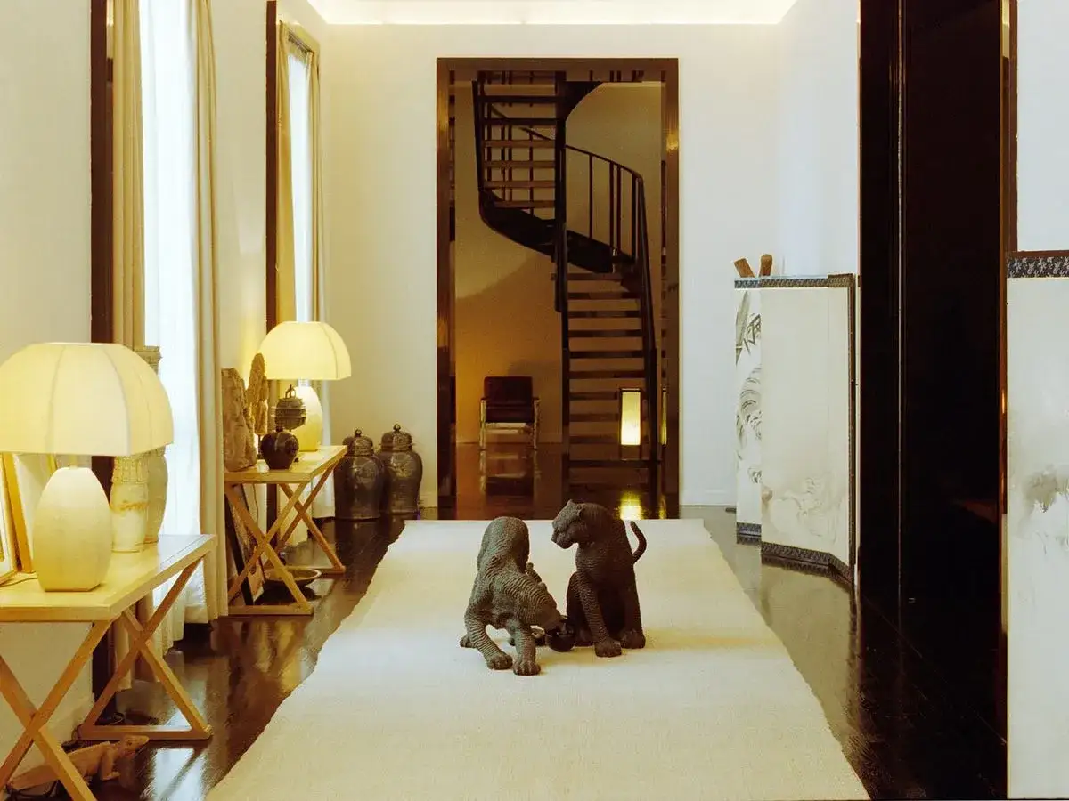 Ingresso elegante della casa Giorgio Armani con sculture di felini, tappeto chiaro, scale a chiocciola e arredi raffinati.