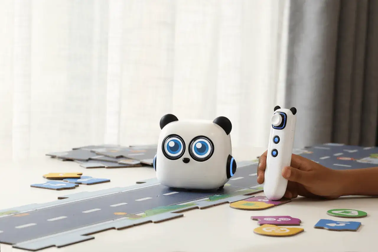 Uroczy robot panda i pilot na stole, otoczone elementami do zabawy, pokazują przyszłość robotów w edukacji.