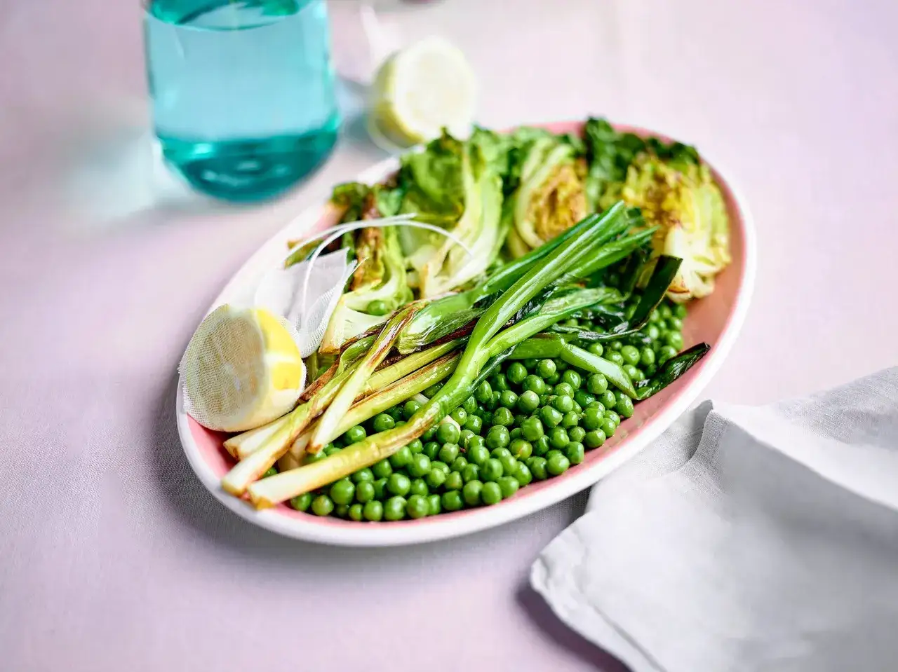 Assiette rose avec petits pois, oignons verts, laitue et citron. Une id&eacute;e pour une recette petit pois fra&icirc;che et l&eacute;g&egrave;re.