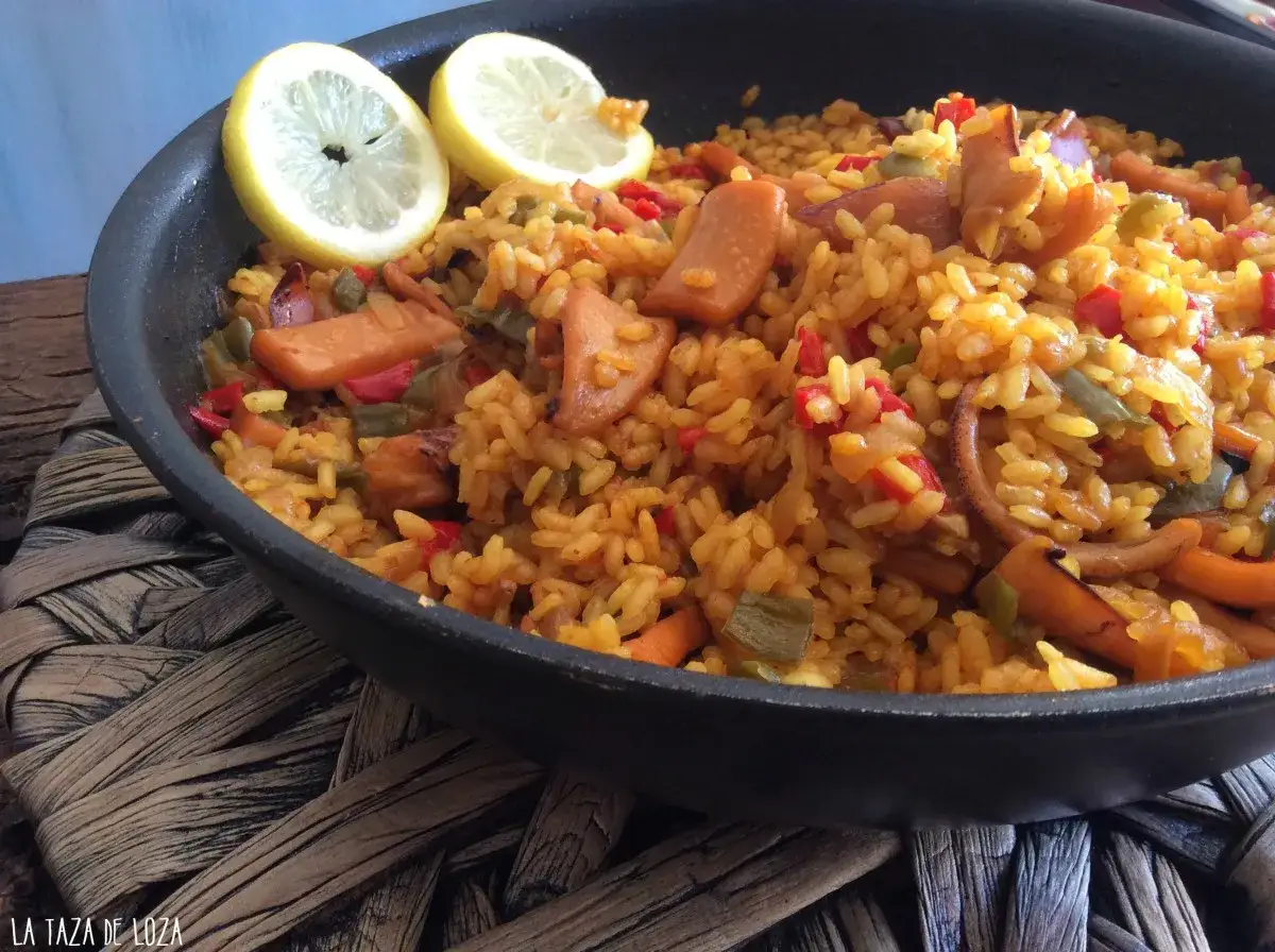 Arroz con calamares en paellera, adornado con rodajas de limón. Un plato lleno de sabor y color.