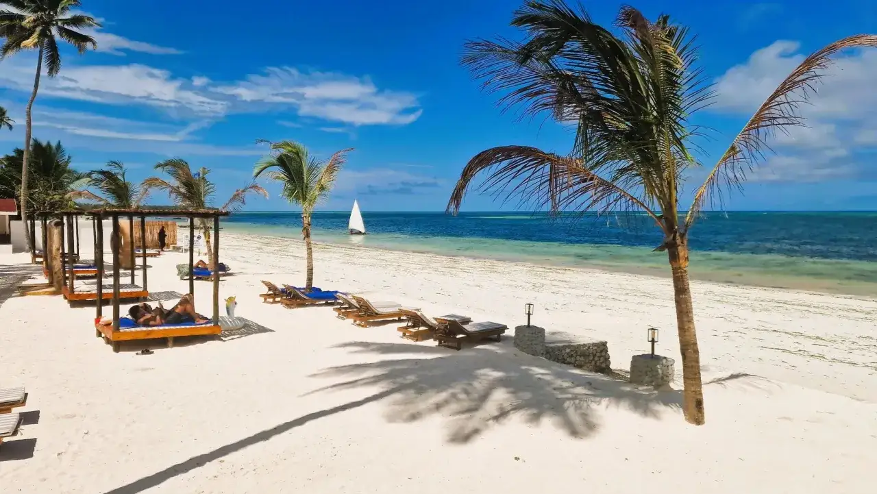 Rajskie plaże, palmy i błękitne morze – idealne miejsce, kiedy na Zanzibarze. Wypoczynek na leżakach pod baldachimami, żaglówka na horyzoncie.