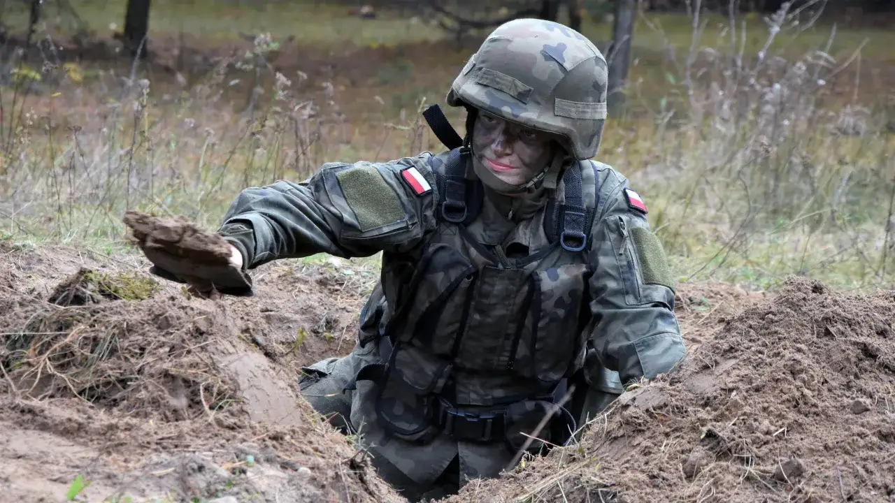 Żołnierz w kamuflażu, z polską flagą na ramieniu, kopie okop. To ważny element wyposażenia, gdy zastanawiasz się, co zabrać na ćwiczenia rezerwy.