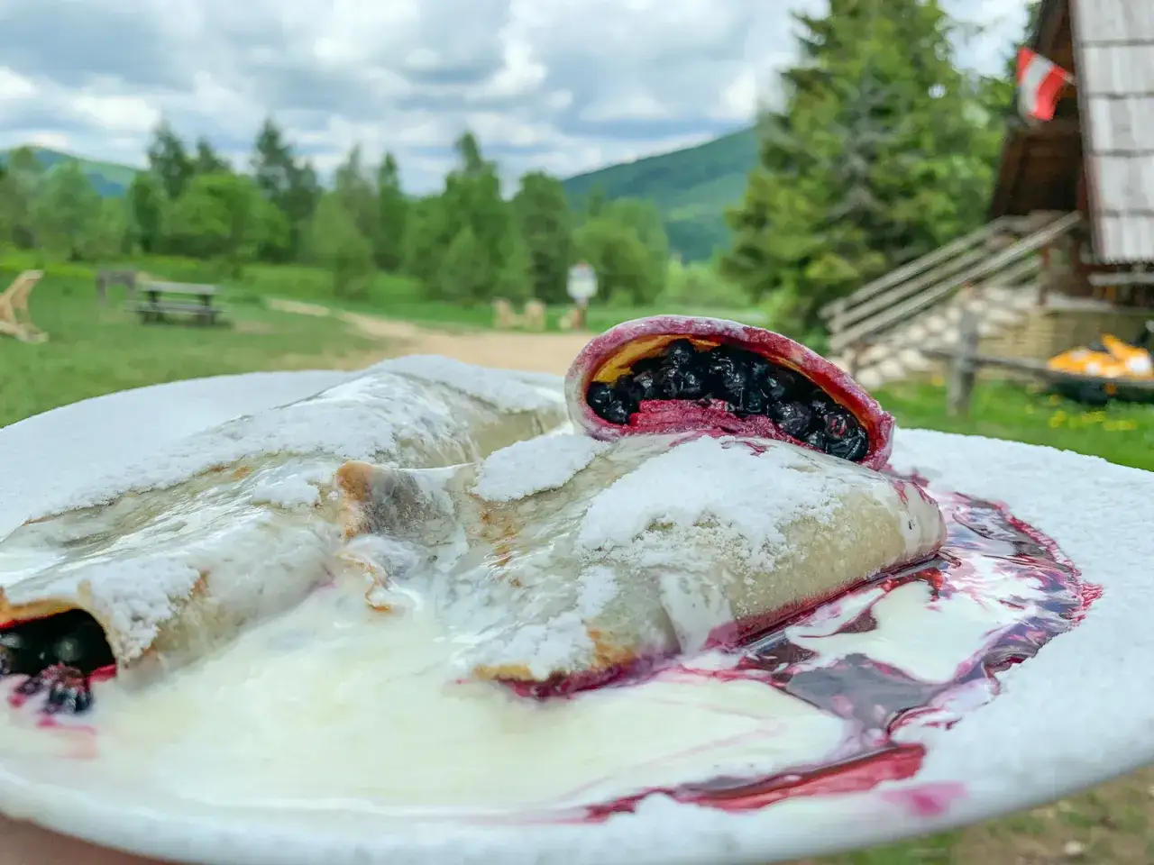 Pyszne naleśniki z jagodami i śmietaną na talerzu, w tle malownicza bac&oacute;wka mała rawka.