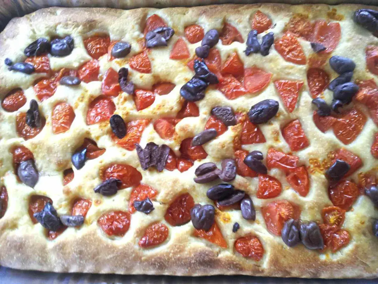 Frisch gebackene Focaccia Pomodoro mit saftigen Tomatenstücken und dunklen Oliven, bereit zum Genießen.