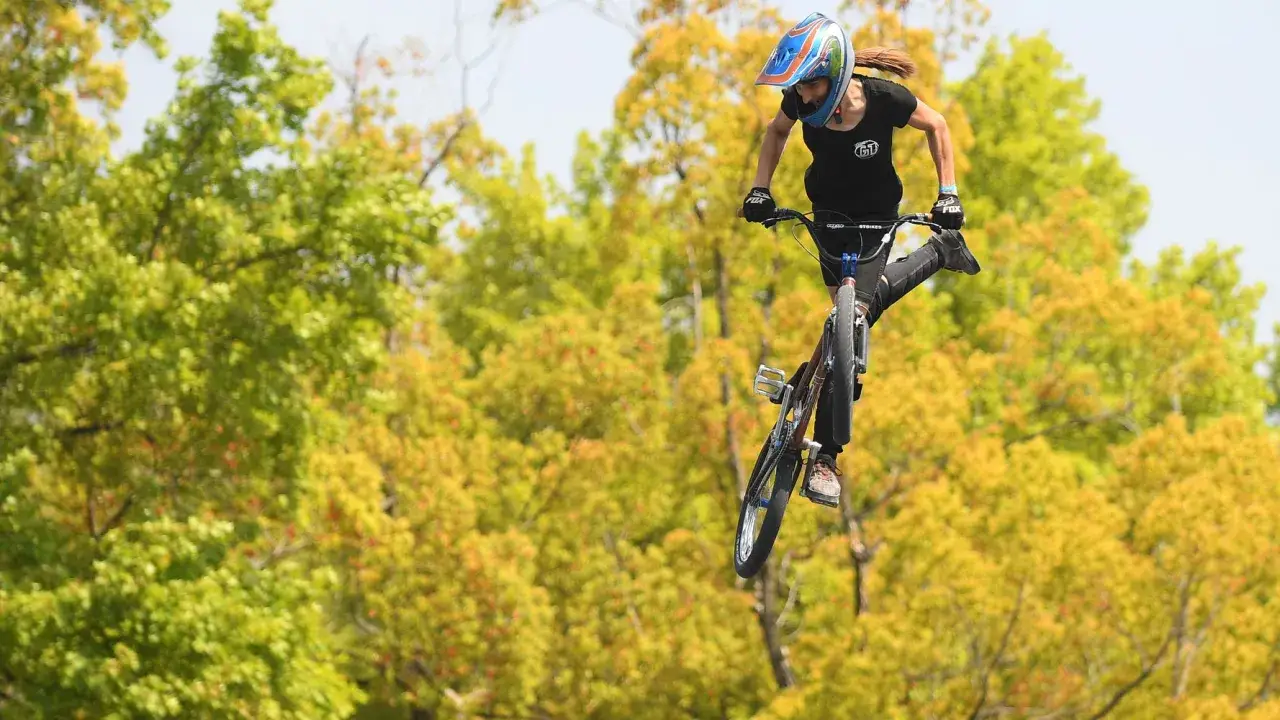 Chelsea Wolfe soars through the air on her bmx bike, performing an epic jump against a backdrop of vibrant autumn trees.