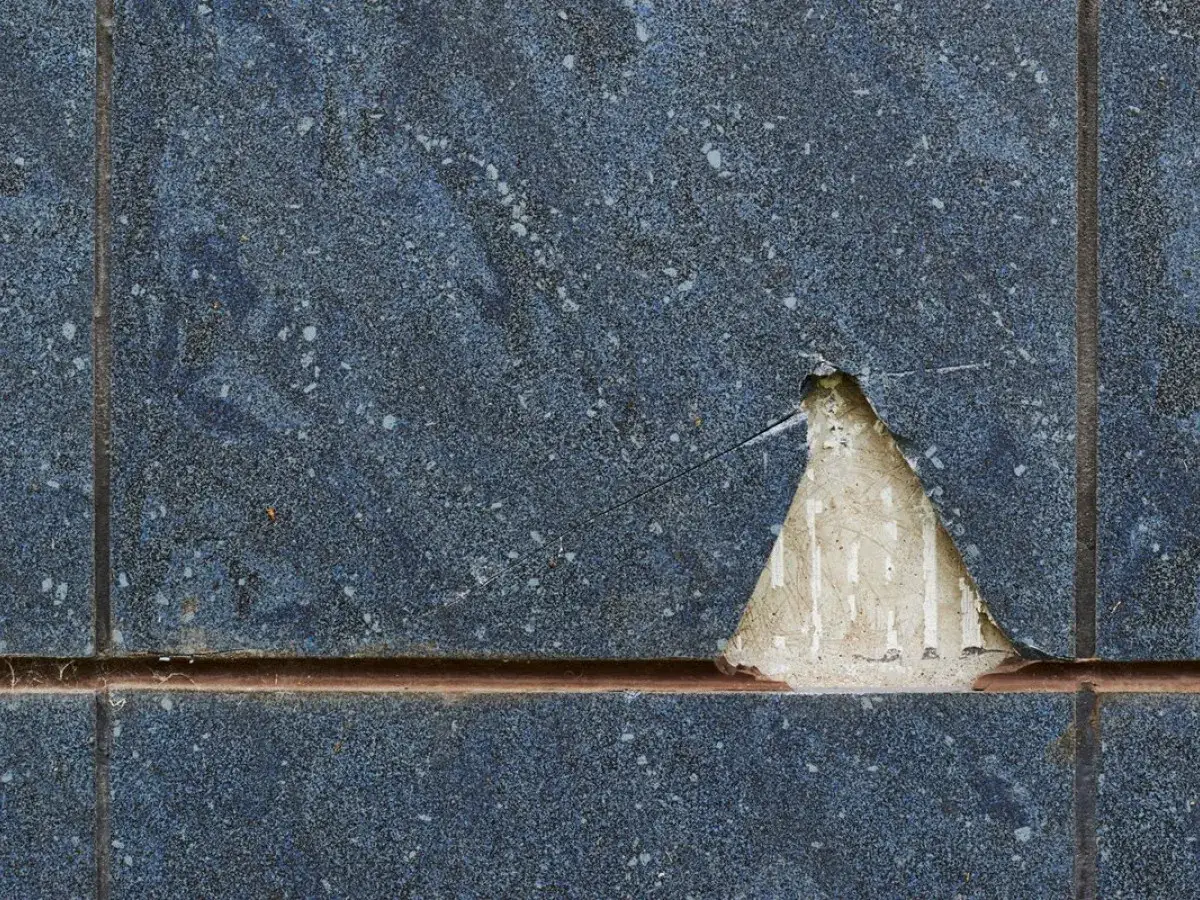 Pękające płytki na ścianie, odsłaniające beton.