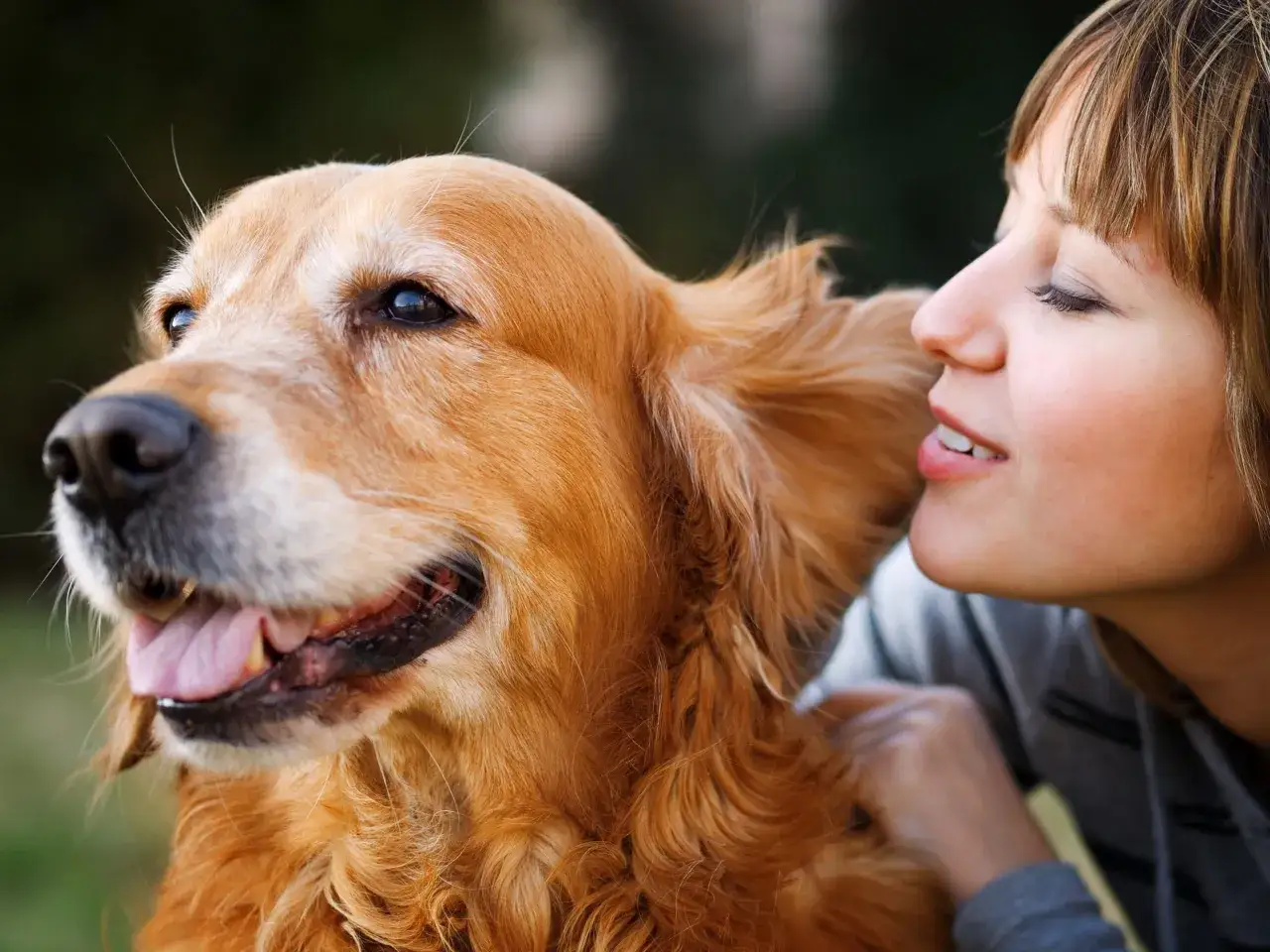 Un golden retriever souriant, la langue sortie, est proche d'une jeune femme. Un moment tendre pour savoir si son chien est heureux.