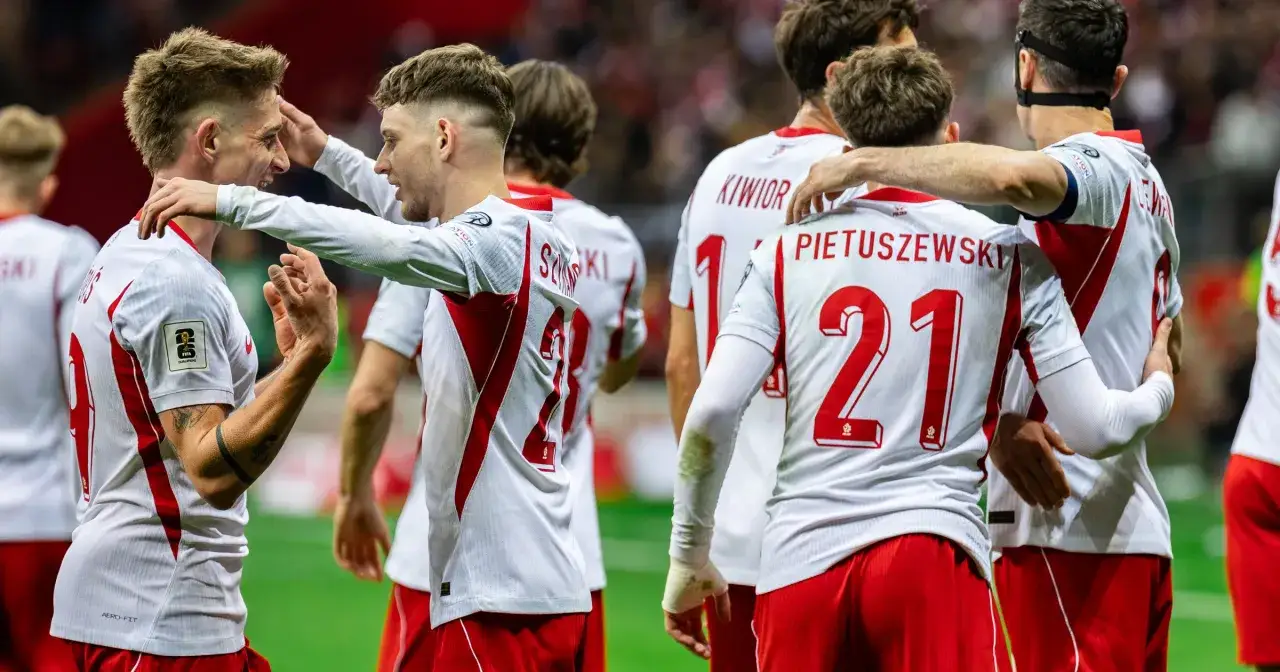 Piłkarze reprezentacji Polski w białych strojach z czerwonymi detalami, z numerami 21 i 9 na plecach, świętują po meczu eliminacji do baraze ms 2026.