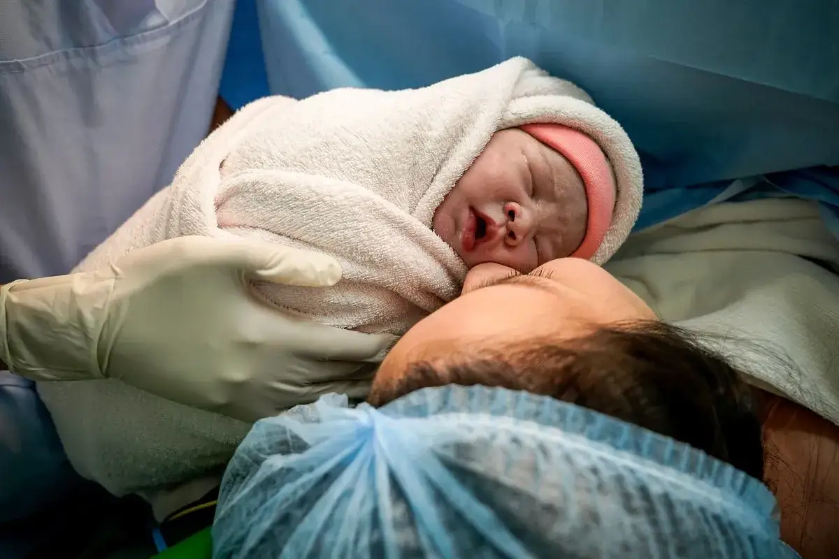 Noworodek owinięty w kocyk przytulony do mamy. Chwila po porodzie naturalnym, pełna miłości i wzruszenia.