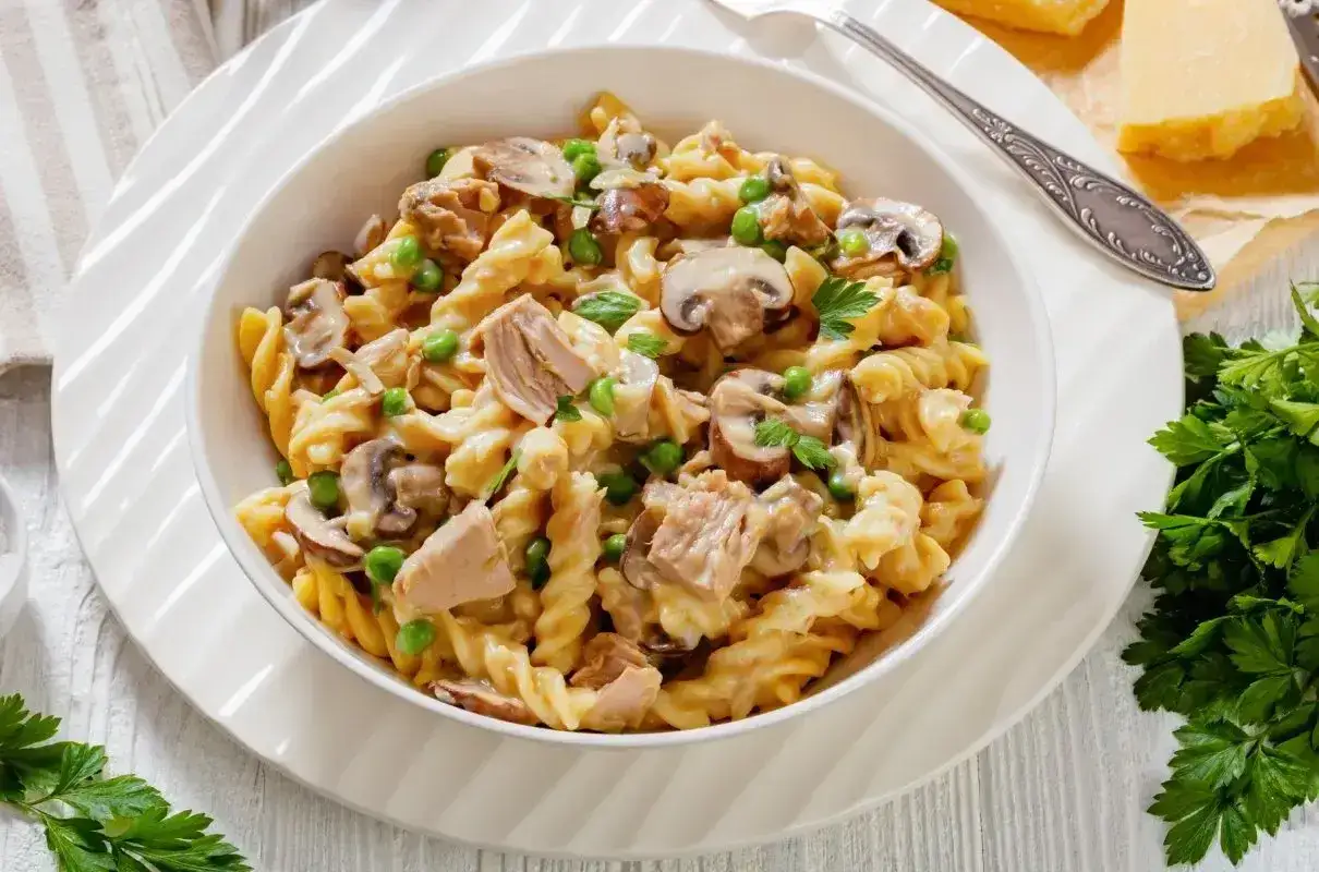 Pyszna fit pasta z tuńczyka z pieczarkami i groszkiem, podana w białej misce, udekorowana natką pietruszki.