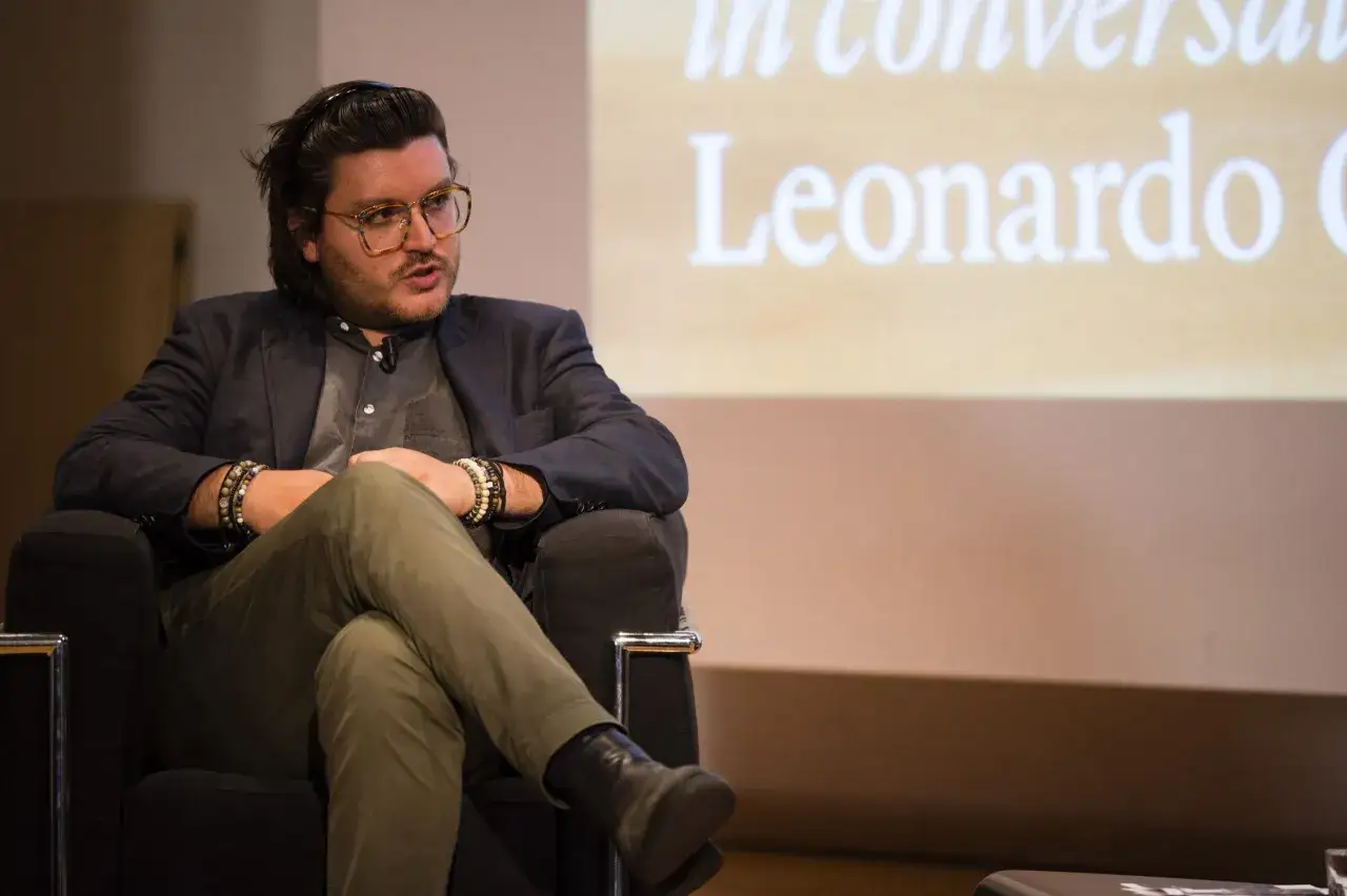 Leonardo Caffo, con occhiali vistosi e bracciali, parla da una poltrona.
