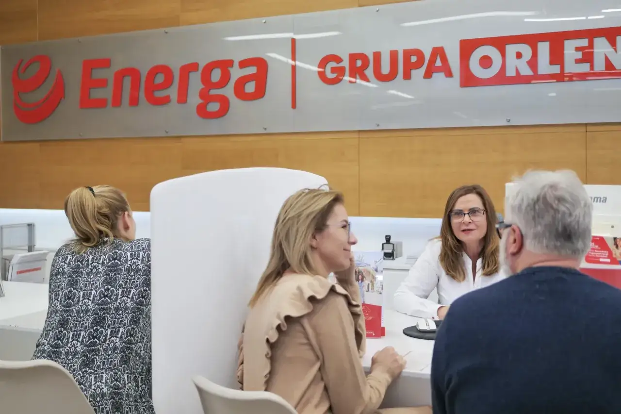 Klienci rozmawiają z pracownicą w punkcie obsługi Grupy Orlen. W tle widoczne logo Energa.