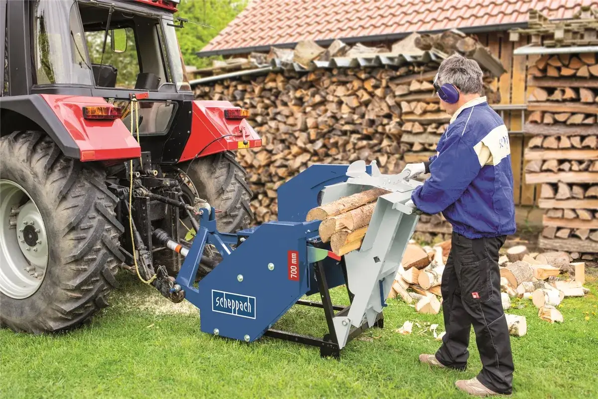 Mann bedient eine Wippsäge, die über die Zapfwelle mit einem Traktor verbunden ist, um Holz zu schneiden.