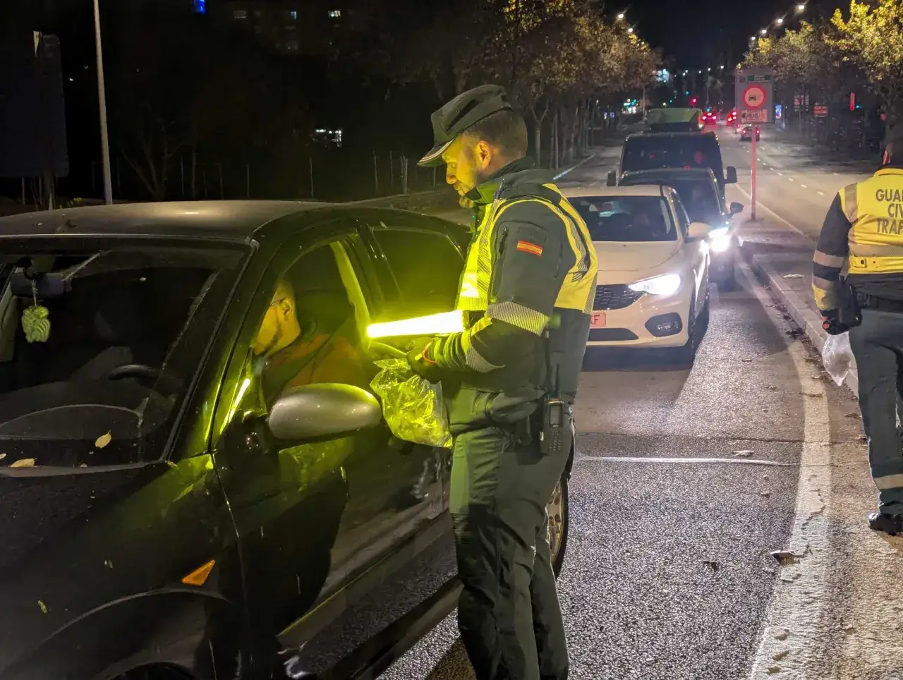 Agente de tr&aacute;fico realiza un control de alcoholemia a un conductor en la carretera de noche.