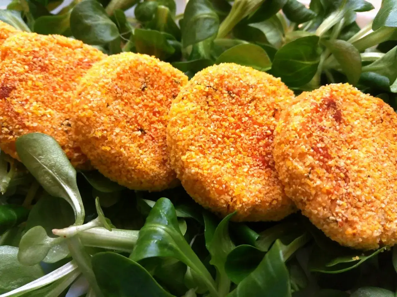 Quattro polpette di lenticchie dorate e croccanti su un letto di insalata fresca.
