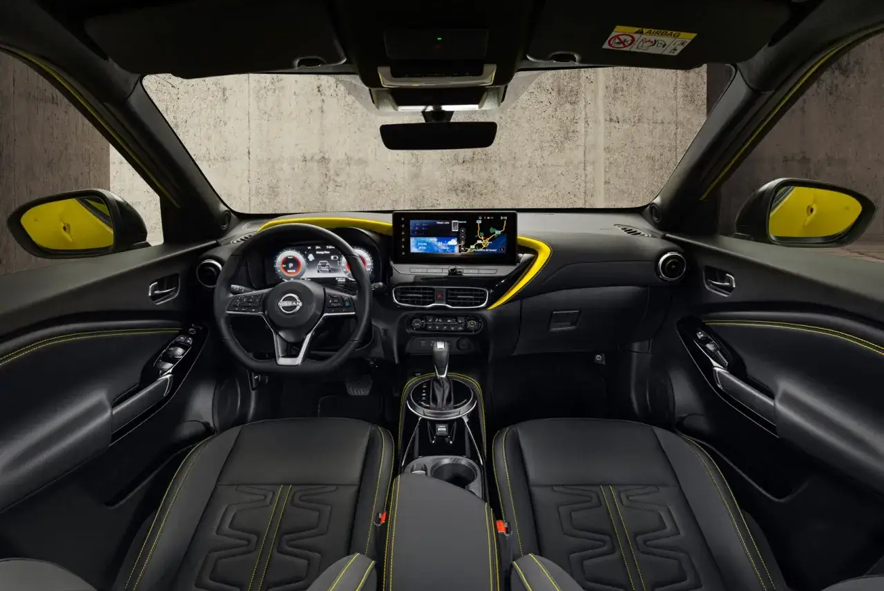 Interiörbild av en Nissan Juke med svarta säten och gula sömmar. Instrumentpanelen har en stor pekskärm och digital instrumentkluster. En spännande Nissan Juke testkörning väntar!